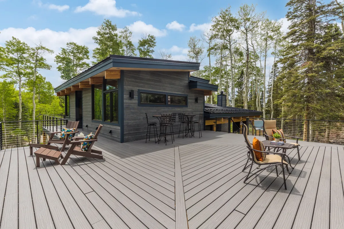 An expansive wooden upper deck set amidst tall trees, furnished with comfortable deck furniture and designed for relaxation and socializing. The setting suggests peaceful sunset views and a seamless connection with the surrounding nature, capturing the tranquil beauty just outside the entertainment loft.