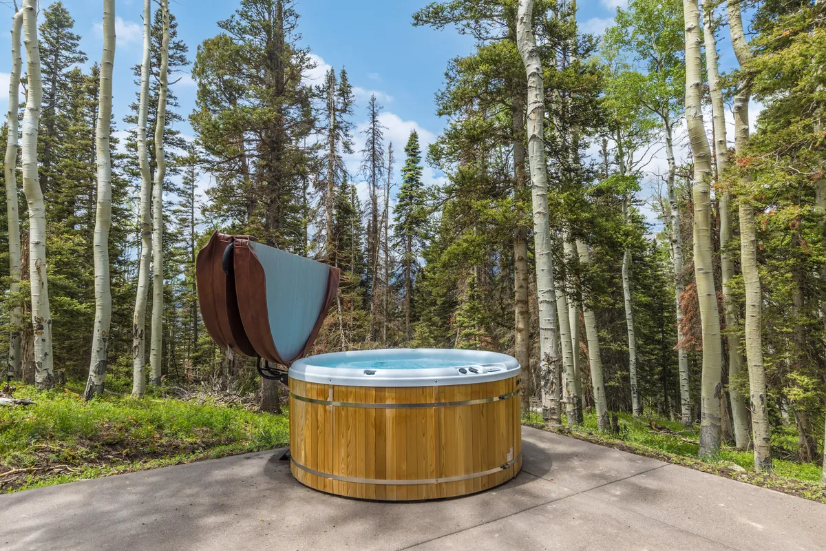 An outdoor hot tub set amidst trees with mountain views, evoking relaxation and connection to nature. The scene suggests a tranquil spot for soaking after a day on the slopes, enhanced by the serenity of the surrounding forest.