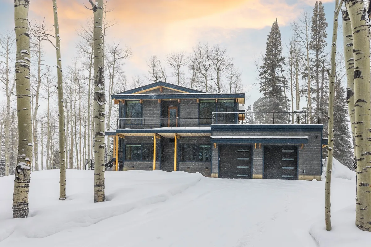 This exterior shot displays the home's modern architecture framed by snow-covered ground, aspen trees, and a spacious balcony. The welcoming façade suggests ample space for large groups and easy access to outdoor adventures, with the mountain environment in full view.