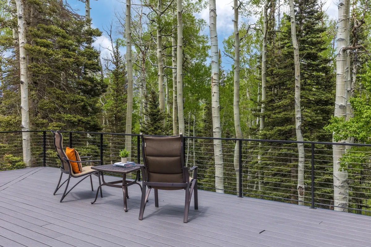 A peaceful wooden deck with chairs and a table, surrounded by lush green trees. The space is perfect for quiet mornings with coffee, reading, or enjoying the seasonal beauty of the forest.
